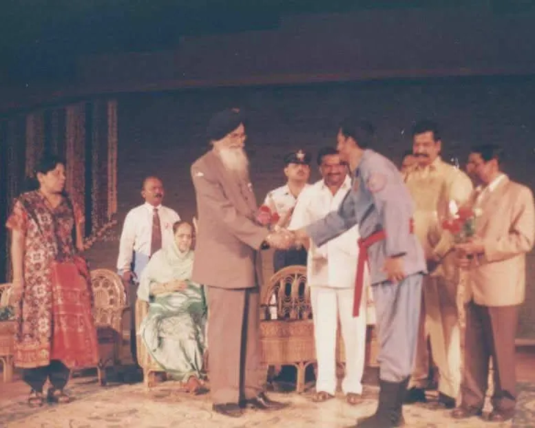 A student in uniform and red belt shaking hands with a dignitary on stage