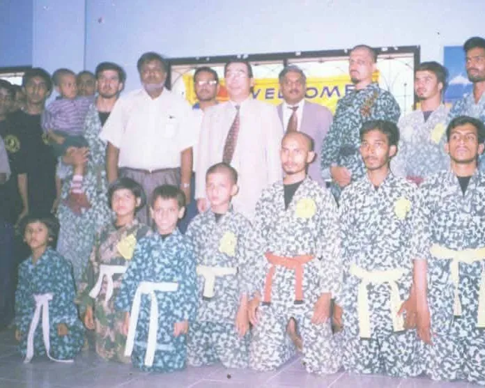 Young students in camouflage gi with white, yellow and orange belts, kneeling with guests